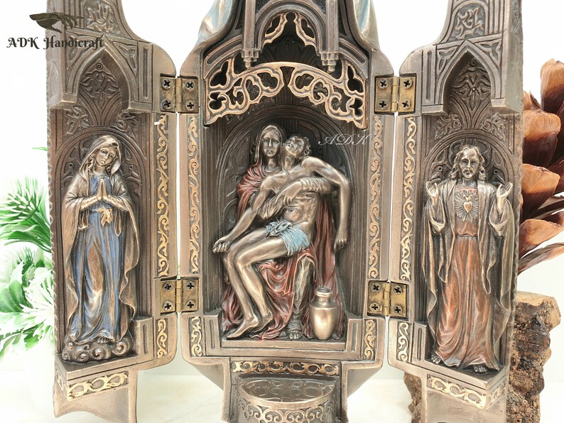 May include: A three-panel wooden altar with a gold-colored finish. The center panel features a sculpture of the Pieta, with Mary holding the body of Jesus. The left panel features a sculpture of Mary, and the right panel features a sculpture of Jesus with his heart exposed.
