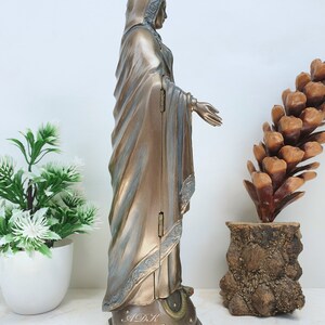 May include: A gold-toned statue of the Virgin Mary, standing on a star-shaped base with the letters "ADK" inscribed. The statue is wearing a crown and a flowing robe.