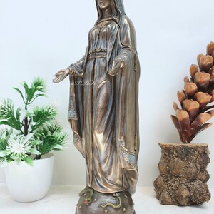 May include: A bronze statue of the Virgin Mary standing on a base with a snake and stars. The statue is wearing a blue robe and a crown. The statue is about 12 inches tall.