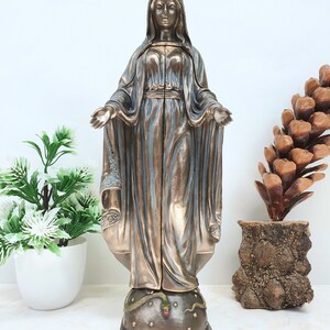 May include: A bronze statue of the Virgin Mary standing on a globe with a snake wrapped around it. The statue is wearing a crown and a blue robe. The globe is decorated with stars.