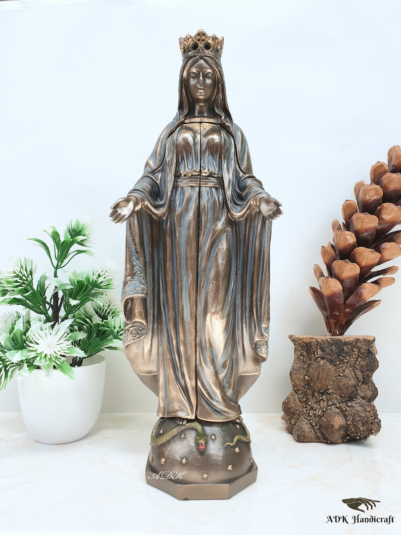 May include: A bronze statue of the Virgin Mary standing on a globe with a snake wrapped around it. The statue is wearing a crown and a blue robe. The globe is decorated with stars.