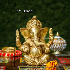 May include: A gold-colored brass statue of Ganesha, the Hindu god of beginnings, prosperity, and good fortune. The statue is 5 inches tall and 4 inches wide. The statue is sitting on a colorful tiled surface.