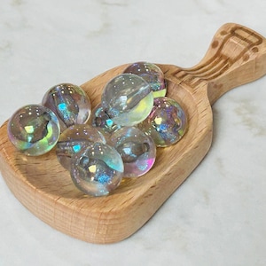 May include: A wooden scoop filled with iridescent glass marbles. The marbles are various shades of blue, green, and purple.