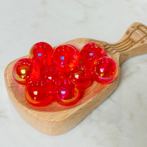 May include: A wooden scoop filled with iridescent red and orange glass beads.