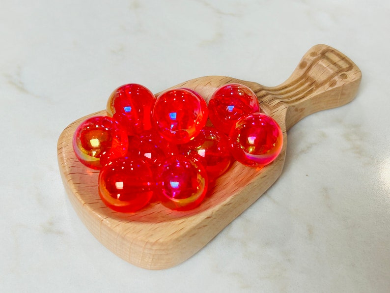 May include: A wooden scoop filled with iridescent red and orange glass beads.