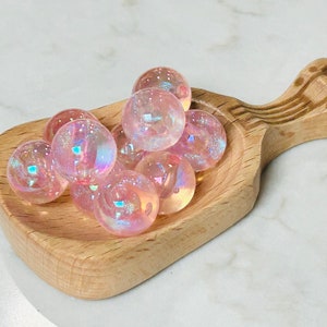 May include: A wooden scoop filled with iridescent pink and white glass beads.
