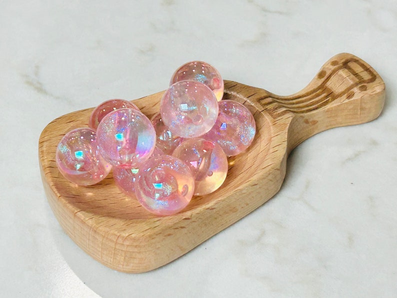 May include: A wooden scoop filled with iridescent pink and white glass beads.