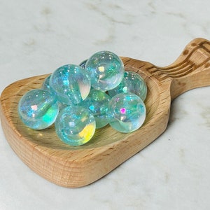 May include: A small wooden scoop filled with iridescent blue glass marbles. The scoop has a carved design on the handle.