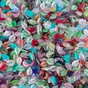 May include: A large collection of small, leaf-shaped beads in a variety of translucent and opaque colors including pink, green, blue, red, and gold. Each bead features a detailed, embossed vein pattern on the surface, creating a textured appearance.