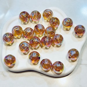 May include: A collection of iridescent glass beads in shades of gold and amber. The beads are round and have a smooth, shiny finish.