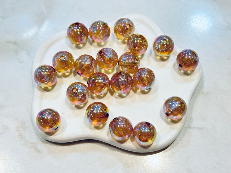 May include: A collection of iridescent glass beads in shades of gold and amber. The beads are round and have a smooth, shiny finish.