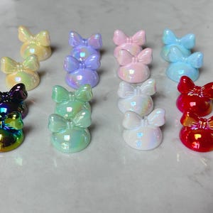 Pu&ograve; includere: Una collezione di abbellimenti a forma di fiocco iridescenti in vari colori, tra cui giallo, viola, rosa, blu, bianco, verde e rosso. I fiocchi sono disposti in file, creando un'esposizione visivamente accattivante.