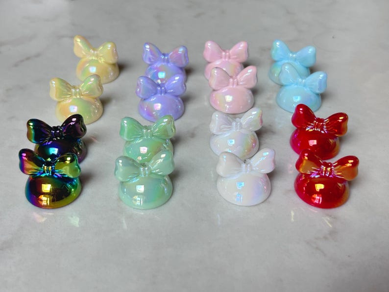 Pu&ograve; includere: Una collezione di abbellimenti a forma di fiocco iridescenti in vari colori, tra cui giallo, viola, rosa, blu, bianco, verde e rosso. I fiocchi sono disposti in file, creando un'esposizione visivamente accattivante.