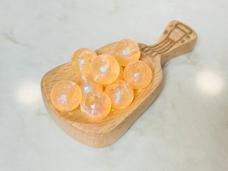 May include: A wooden scoop filled with iridescent orange glass beads