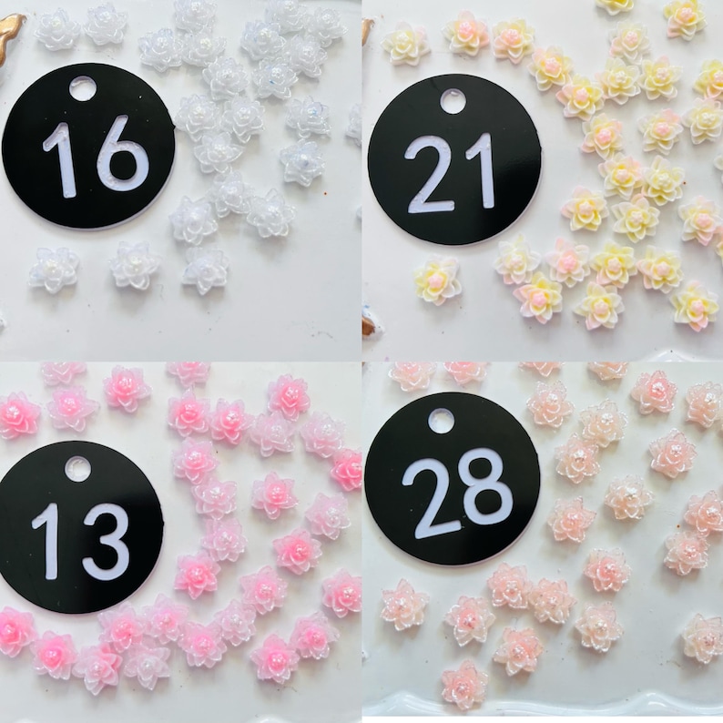 May include: A collection of small, multi-petaled flower cabochons with central beads, organized into four groups labeled with black circular tags numbered 16, 21, 13, and 28. The flowers appear in white, yellow-pink, light pink, and peach tones.