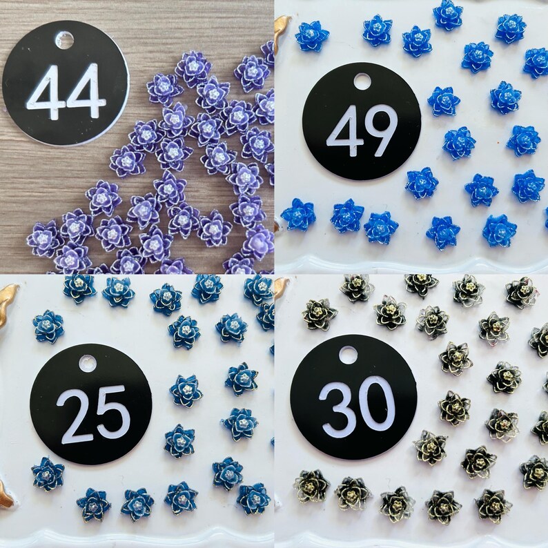 May include: A collection of small flower-shaped embellishments in four color groups, each labeled with a circular black tag featuring white numbers 44, 49, 25, and 30. The flowers are purple, bright blue, teal, and metallic silver-toned.