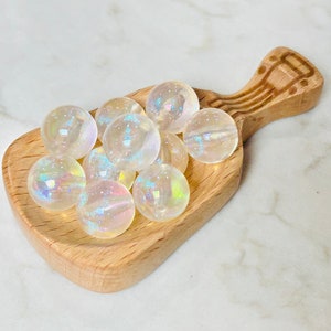 May include: A wooden scoop filled with iridescent white glass beads. The beads are round and have a rainbow sheen.