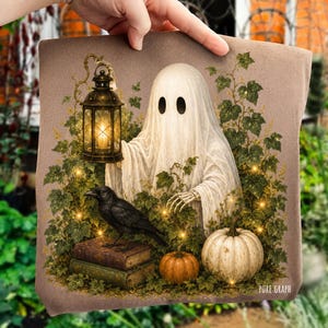 May include: A brown t-shirt featuring a graphic of a white ghost holding a lit lantern, a black crow perched on two stacked books, and two pumpkins surrounded by green ivy leaves. The text Pure Graph is printed in the bottom right corner.