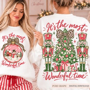 Può includere: Una felpa bianca con la grafica di una pallina di Natale con un pupazzo di neve e casette, e sul retro un albero di Natale con due schiaccianoci, regali e un fiocco leopardato, con il testo It's the most wonderful time.