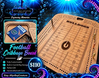 May include: A wooden cribbage board designed like a football field with the word BULLDOGS and a G logo engraved on the surface. The board features rows of holes for scoring, metal pegs, and a storage compartment containing a deck of playing cards.