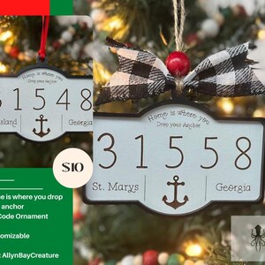 May include: A blue and white wooden ornament shaped like a sign with the text "Home is where you drop your anchor" and the zip code "31558" with the words "St. Marys" and "Georgia" below the numbers. The ornament has a black anchor symbol and a black and white checkered bow.