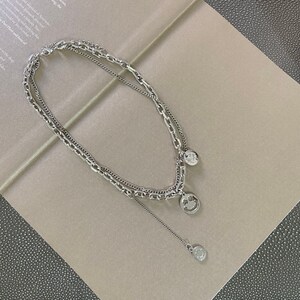 May include: Silver layered chain necklace with three smiley face charms. The necklace has a delicate chain with a smaller smiley face charm dangling from it.