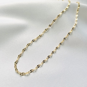 Puede incluir: Delicado collar de oro con un diseño de eslabones ovalados repetidos. El collar se muestra sobre una superficie blanca texturizada, resaltando su brillo sutil y su elegancia discreta. Una fina pieza de joyería adecuada para el uso diario o ocasiones especiales.