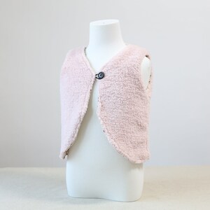 May include: A pink faux fur waistcoat with a single button fastening. The waistcoat is sleeveless and has a curved hem.