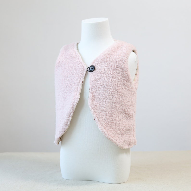 May include: A pink faux fur waistcoat with a single button fastening. The waistcoat is sleeveless and has a curved hem.