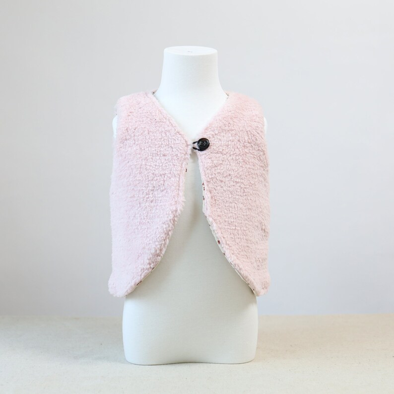 May include: A pink faux fur waistcoat with a single button fastening. The waistcoat is sleeveless and has a soft, fluffy texture.