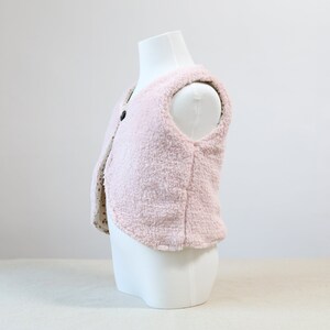 May include: A pink fleece vest with a button fastening. The vest is sleeveless and has a soft, fluffy texture.