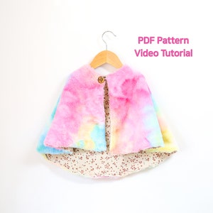 May include: A tie-dye faux fur cape with a brown button closure. The cape is hanging on a wooden hanger against a white background. The text "PDF Pattern Video Tutorial" is displayed above the cape.
