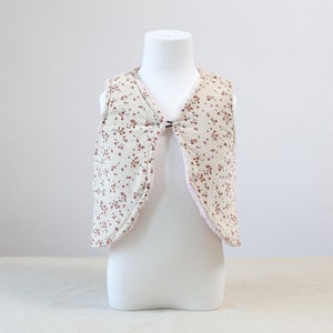 May include: A cream-coloured vest with a pink lining and a small floral pattern in shades of brown and pink.