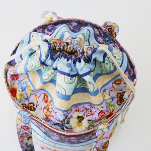 K&ouml;nnte beinhalten: Eine bunte Kordeltasche mit floralem und geometrischem Muster. Die Tasche hat einen wei&szlig;en Kordelzug und ist aus Stoff.