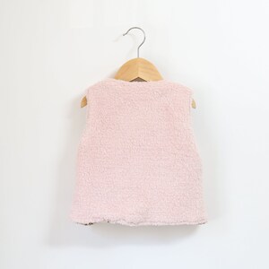May include: A pink fleece vest with no sleeves hanging on a wooden hanger.