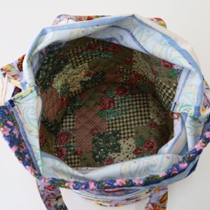 K&ouml;nnte beinhalten: Eine blaue und wei&szlig;e Stofftasche mit Blumendruck und Kordelzug. Das Innere der Tasche ist mit einem Patchwork-Stoff ausgekleidet, der verschiedene Blumen- und Karomuster aufweist.