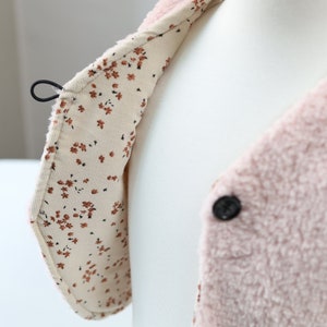 May include: A pink fleece jacket with a floral patterned lining. The jacket has a button closure and a loop on the collar.