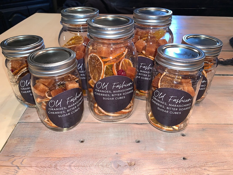 May include: Six glass jars filled with dried orange slices, maraschino cherries, and sugar cubes. Each jar has a black label with the text "Old Fashion" and a list of ingredients.