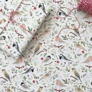 May include: White wrapping paper with a repeating pattern of birds, berries and leaves. The birds are white with black accents and are depicted in various poses. The berries are red and the leaves are green.