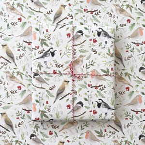 May include: White wrapping paper with a repeating pattern of birds, flowers and berries. The birds are in various poses, including flying, perched and singing. The flowers are white and pink, and the berries are red. The paper is tied with a red and white string.