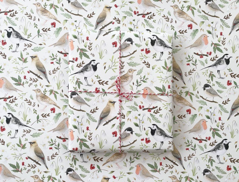 May include: White wrapping paper with a repeating pattern of birds, flowers and berries. The birds are in various poses, including flying, perched and singing. The flowers are white and pink, and the berries are red. The paper is tied with a red and white string.