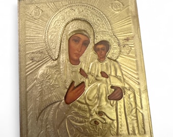 May include: A gold-toned religious icon depicting a mother and child. The figures are in detailed relief, with halos and ornate clothing. The background features radiating lines, and the overall design is rectangular.