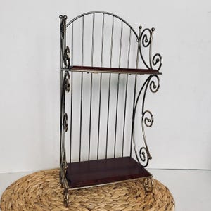 May include: A decorative, two-tiered shelf with a dark metal frame and dark wood shelves. The frame has an arched top and decorative scrollwork on the sides. The shelves are rectangular.