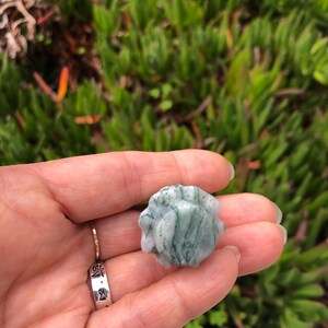 May include: A green and white agate stone with a swirling pattern. The stone is smooth and polished.