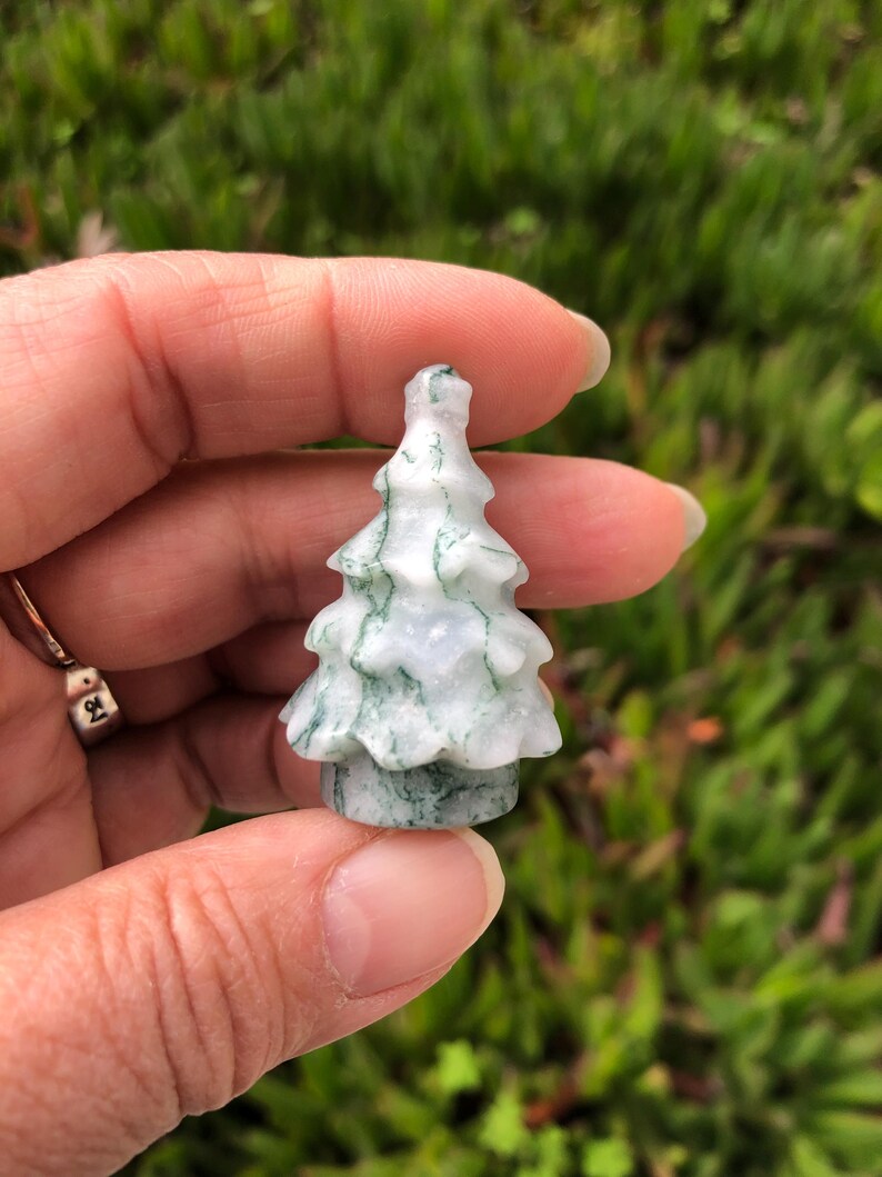 May include: A small, white and green carved agate tree ornament. The tree is carved in a simple, traditional style with a rounded top and a few branches.