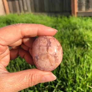May include: A smooth, polished pink and white agate stone with a swirling pattern. The stone is about the size of a golf ball.