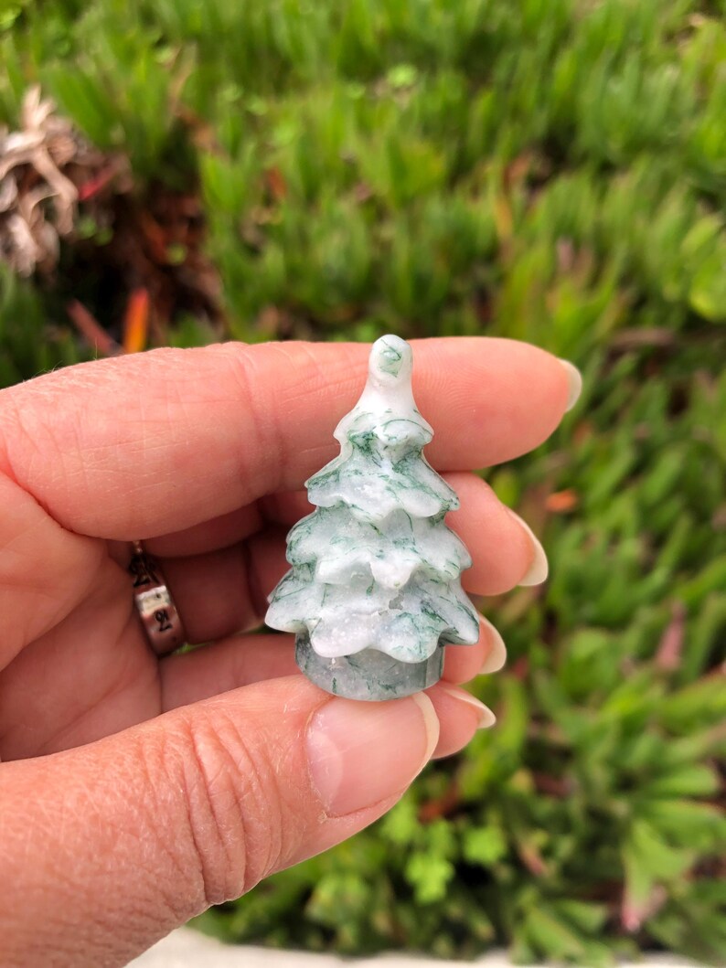 May include: A small, green and white carved jade tree ornament. The tree is about 2 inches tall and has a detailed, realistic design.