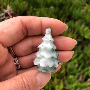 May include: A small, carved green and white jade tree ornament. The tree is about 2 inches tall and has a detailed, realistic design.