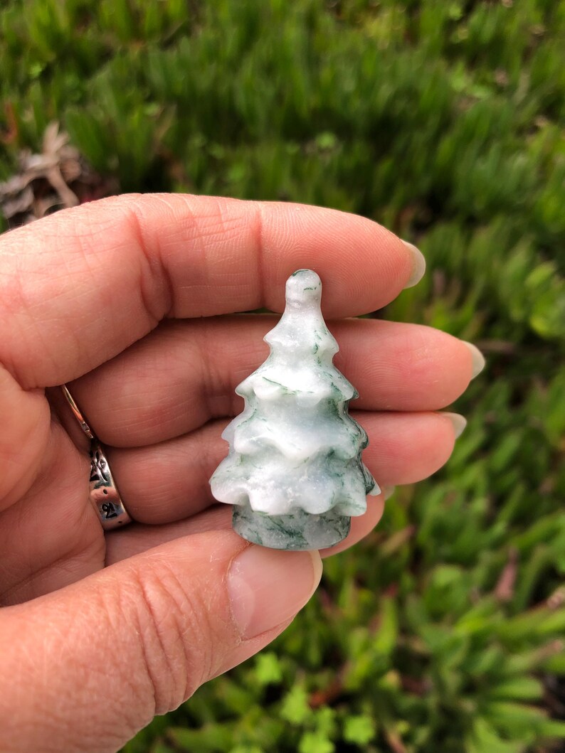 May include: A small, carved green and white jade tree ornament. The tree is about 2 inches tall and has a detailed, realistic design.