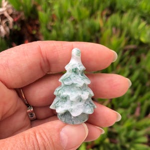 May include: A small, carved green and white agate tree ornament. The tree is about 2 inches tall and has a detailed, realistic design.